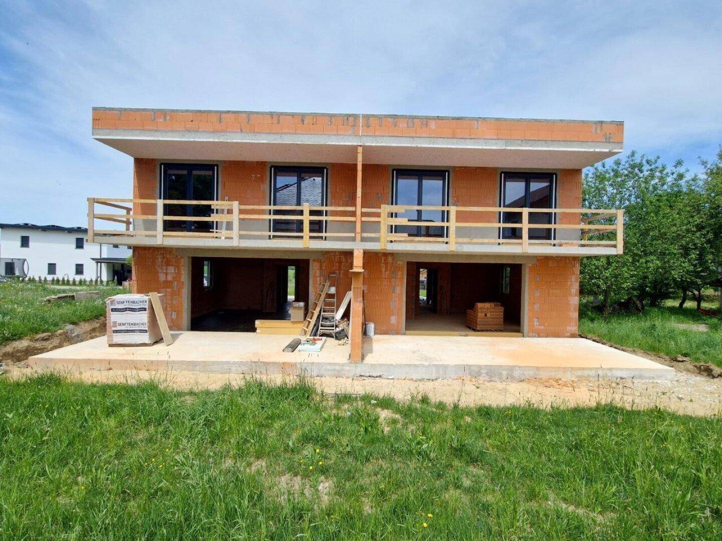 Frontansicht des Doppelhauses im Rohbau mit Balkonen und großen Fensterfronten.