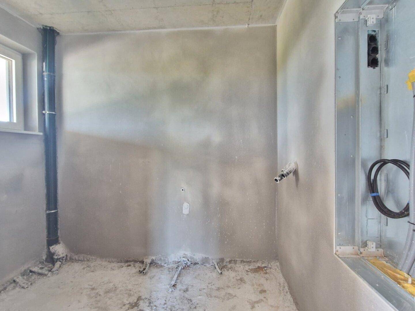 Rohbau eines Funktionsraums mit sichtbaren Installationen und kleinem Fenster.