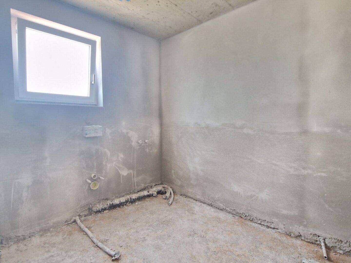 Rohbau eines Badezimmers mit Fenster und Vorinstallationen für Sanitäranlagen.