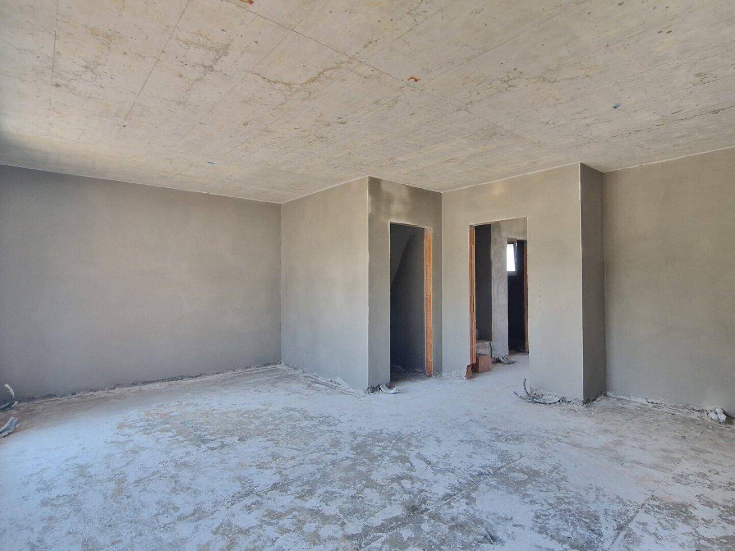 Unfertiger Innenraum mit verputzten Wänden und Rohbetondecke, bereit für den weiteren Ausbau.