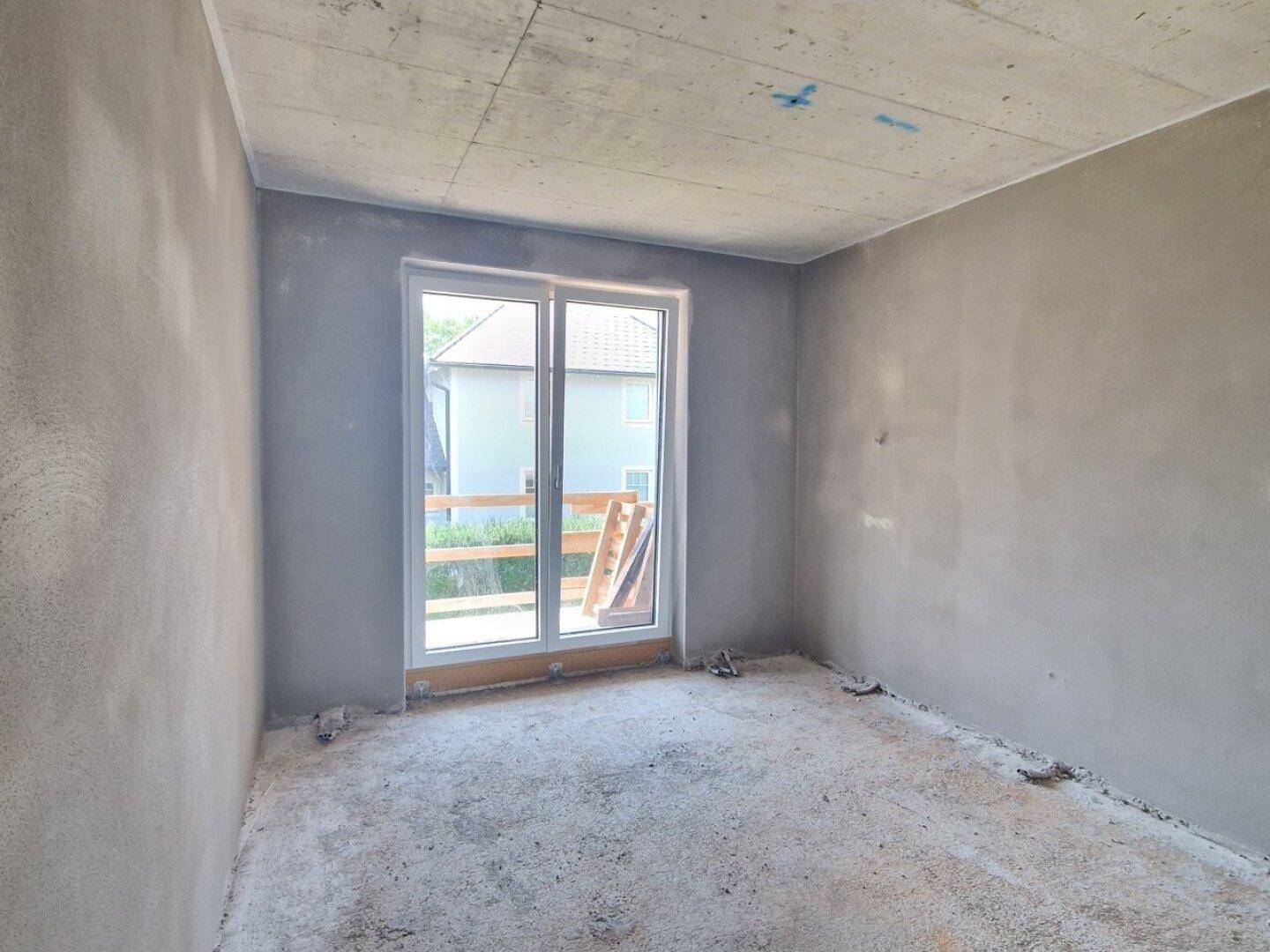 Rohbau-Schlafzimmer mit Schiebetür zum Außenbereich und Blick auf benachbarte Häuser.