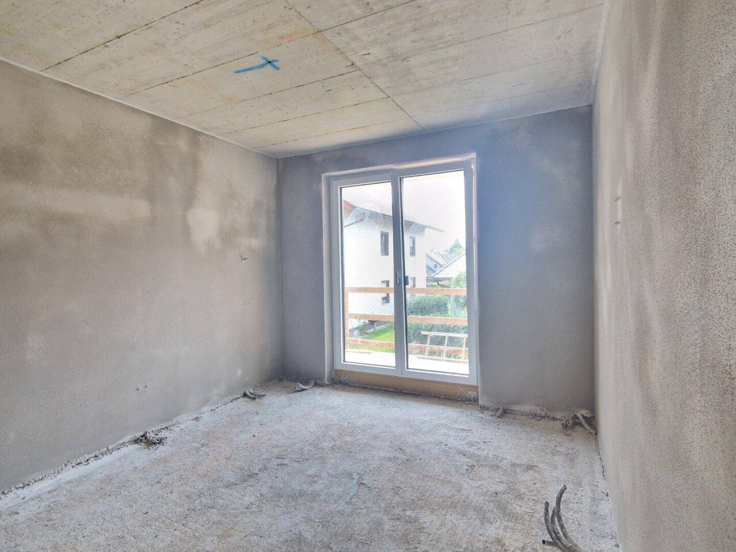 Unfertiges Schlafzimmer mit großem Fenster und Zugang zu einem potenziellen Balkon oder Terrasse.