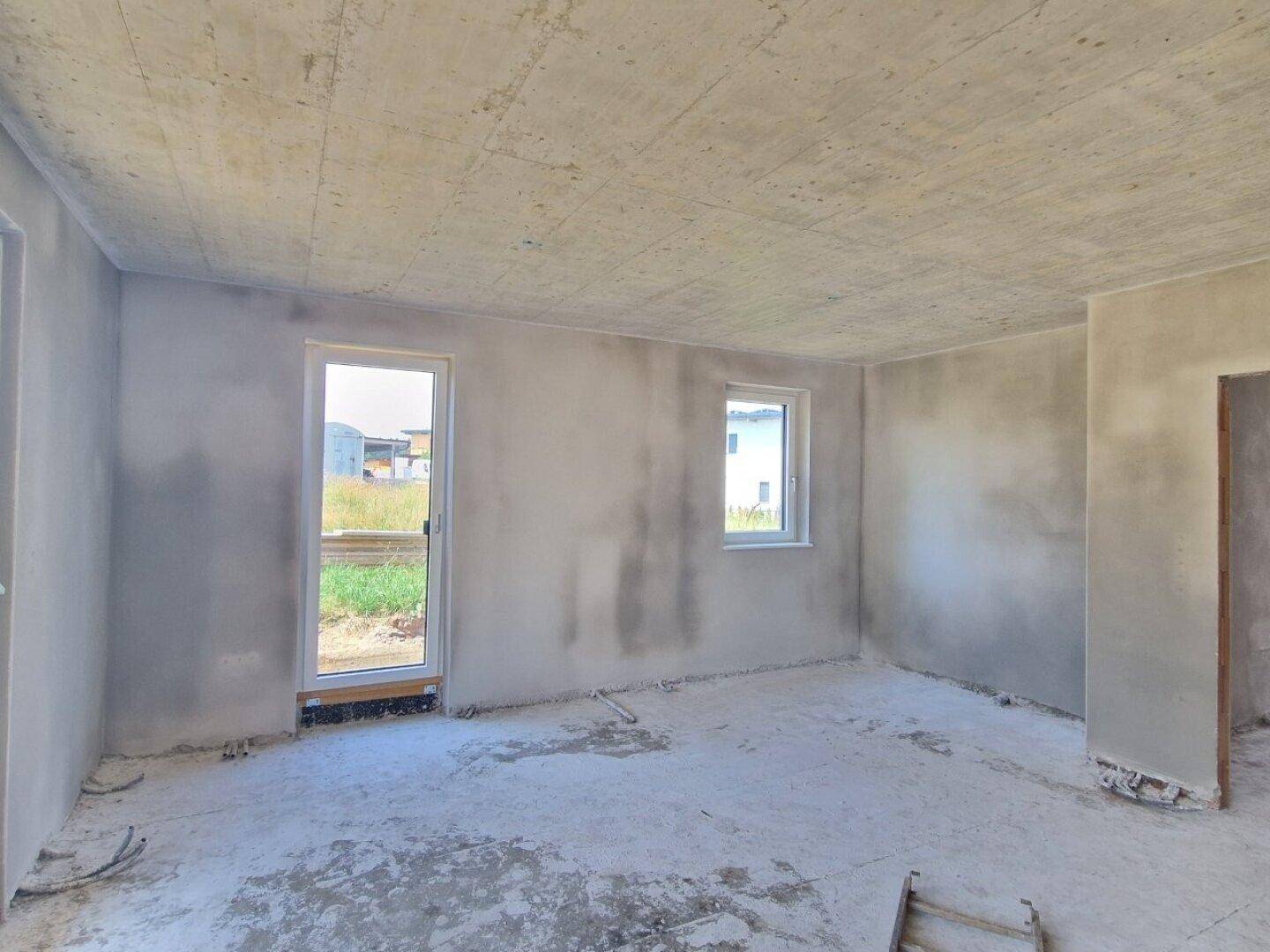 Rohbau eines Zimmers mit Fenster und Tür zum Außenbereich, wartet auf den Innenausbau.
