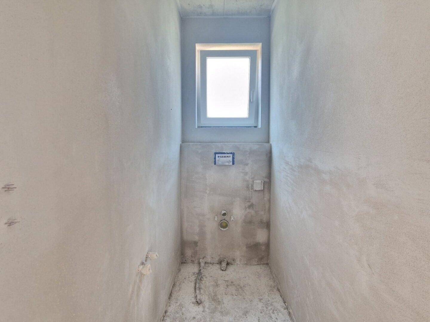 Kleiner Raum im Rohbau mit Fenster und Vorinstallationen für ein WC.