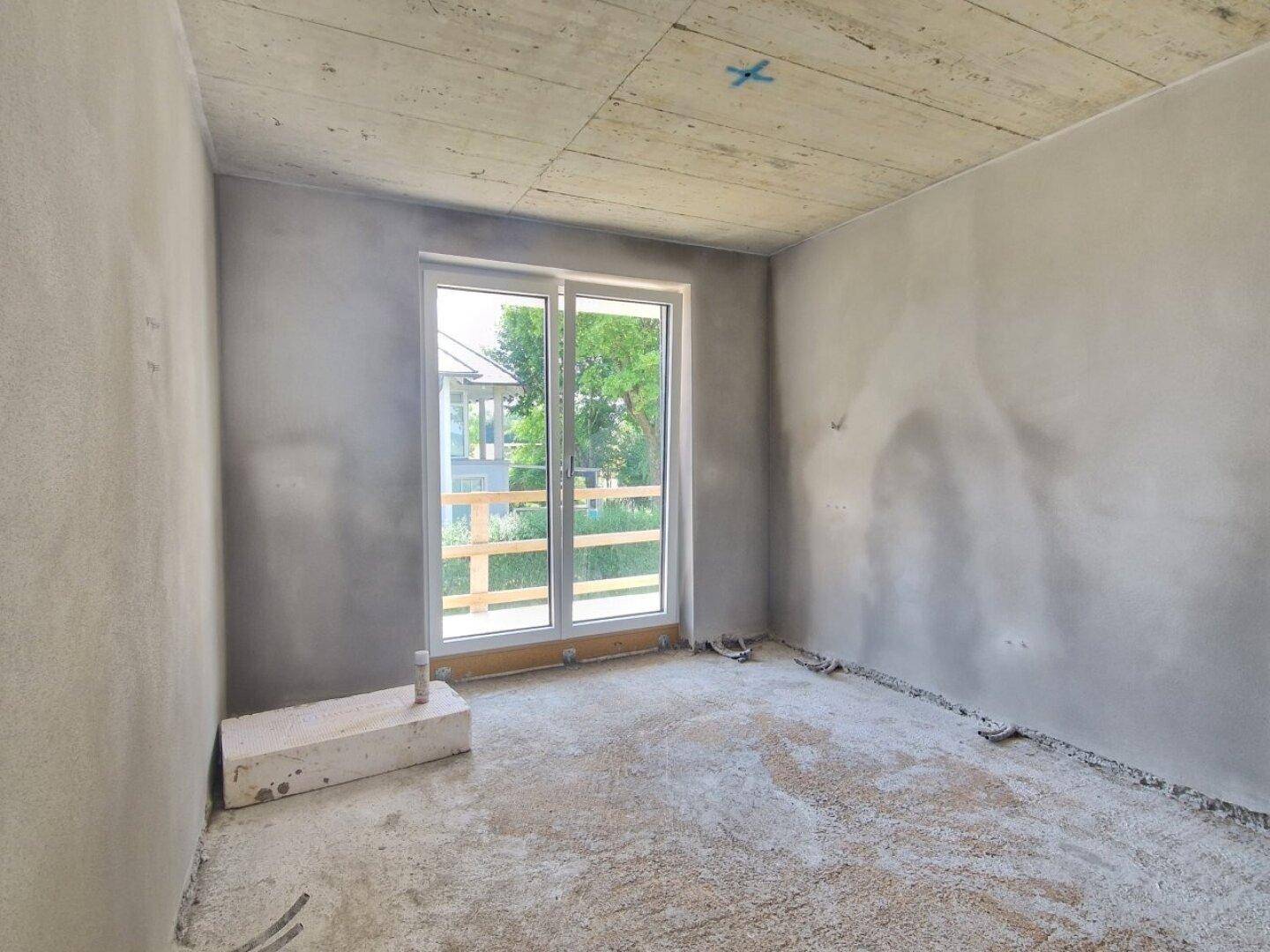 Unfertiger Raum mit großer Fenstertür und Blick auf die Umgebung, bereit für den Ausbau.