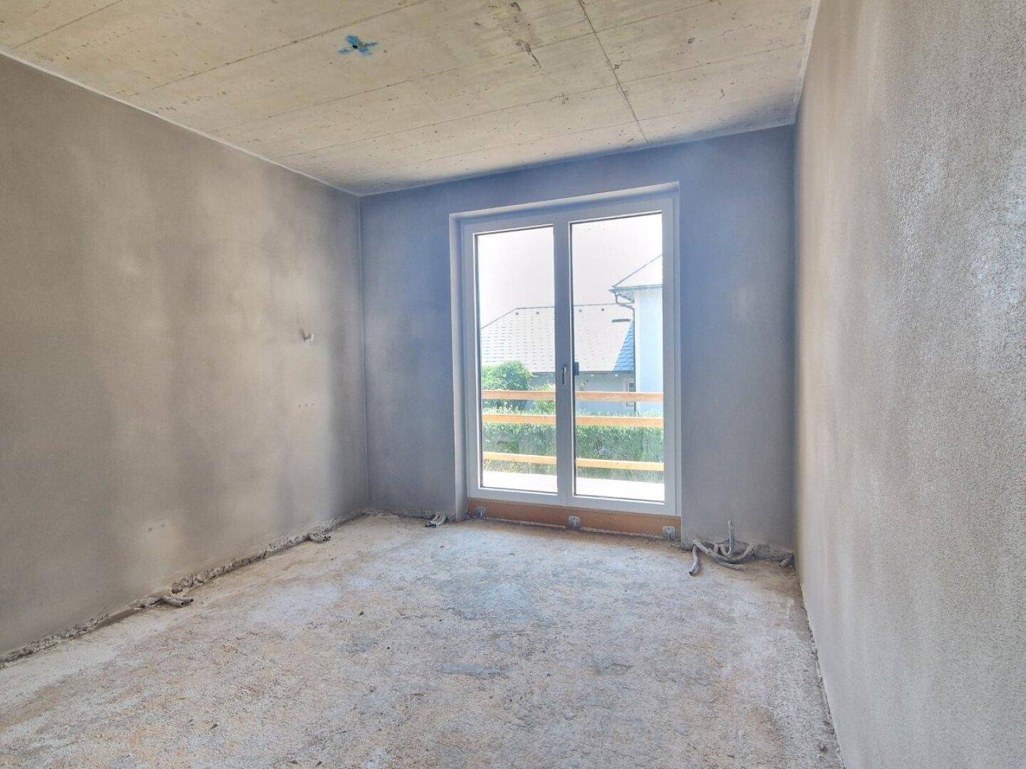 Rohbau eines Zimmers mit großer Fenstertür, die viel Tageslicht hereinlässt.
