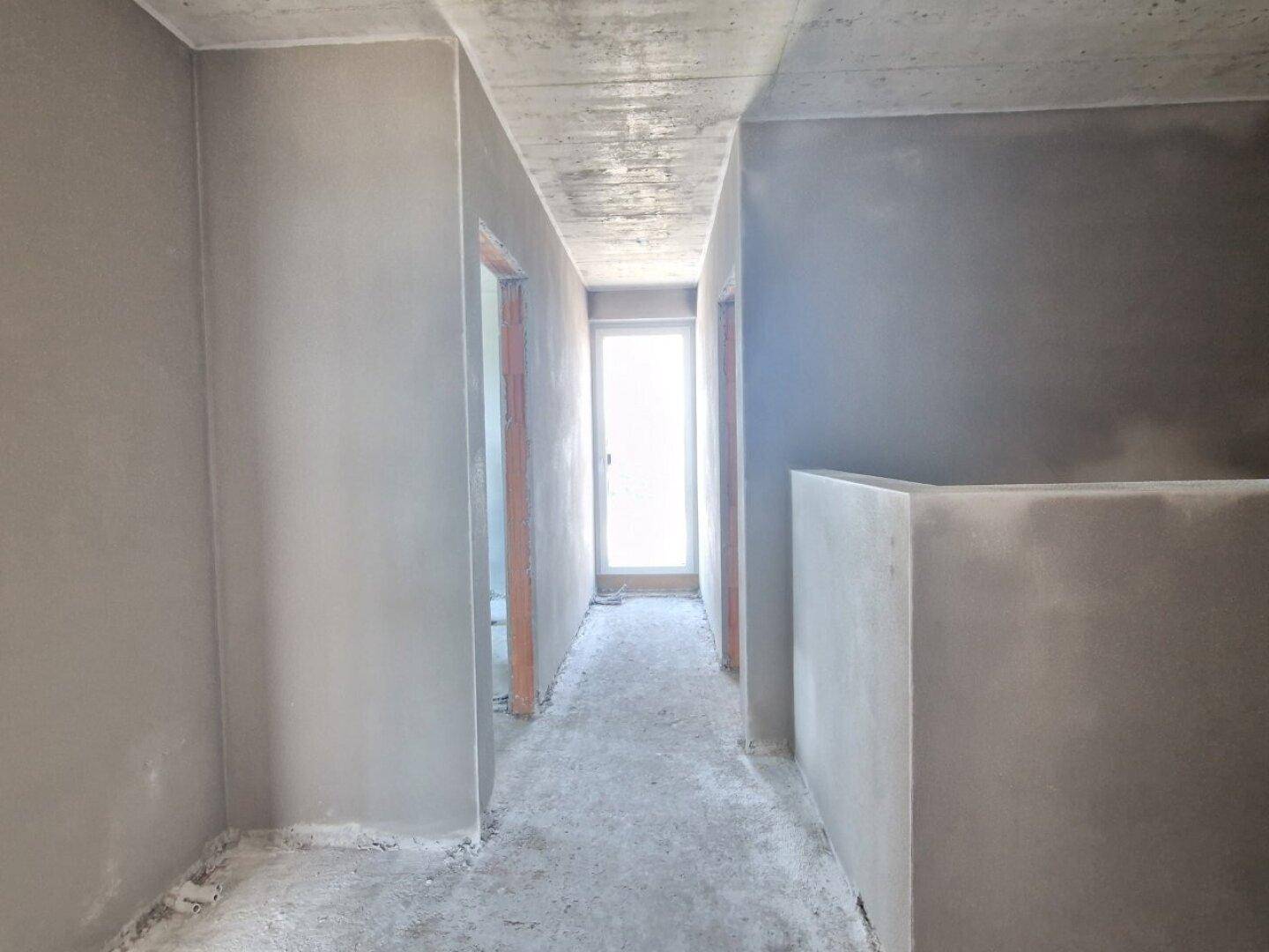 Langer Flur im Rohbau mit Fenster am Ende, der die Räume verbindet.