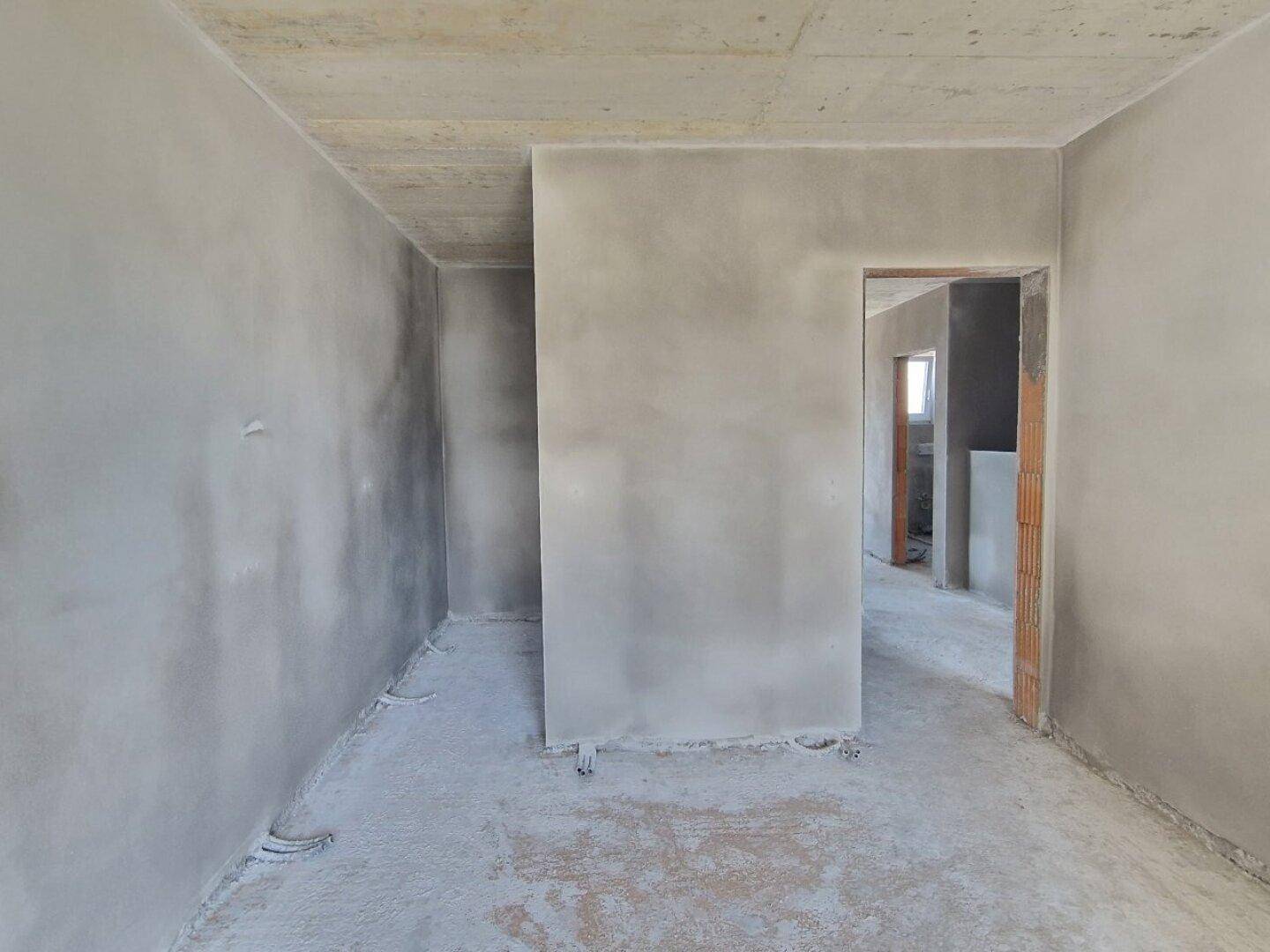 Unfertiger Innenraum mit Türöffnung zu einem weiteren Bereich, wartet auf den Innenausbau.