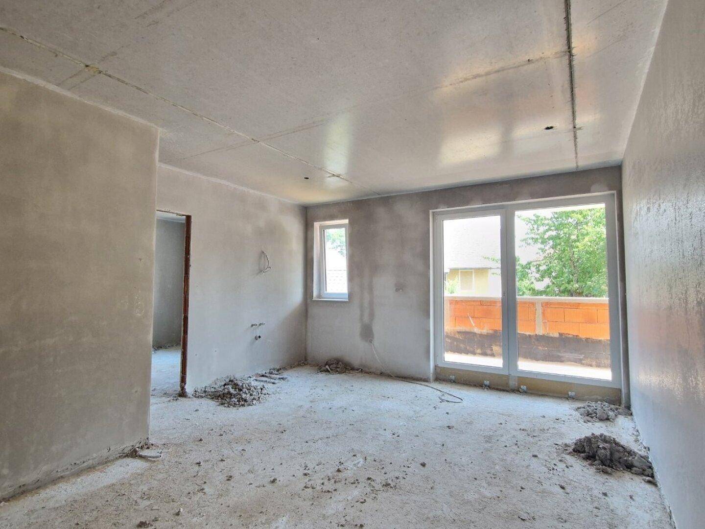 Rohbau-Innenraum mit Zugang zu einem Balkon und einem Fenster, viel natürliches Licht.