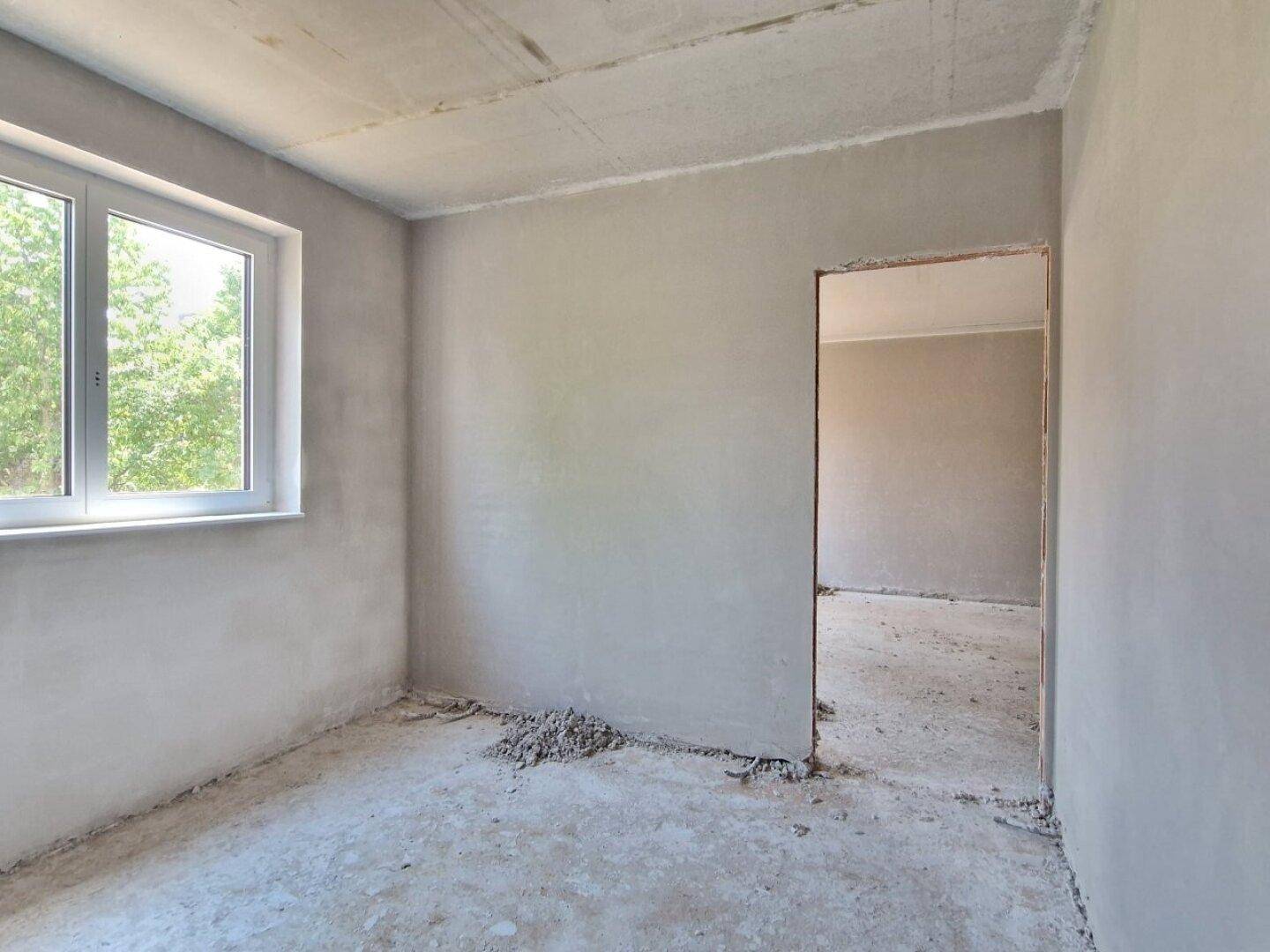Rohbau-Innenraum mit Fenster und Türöffnung, die den Blick in einen weiteren Raum freigibt.