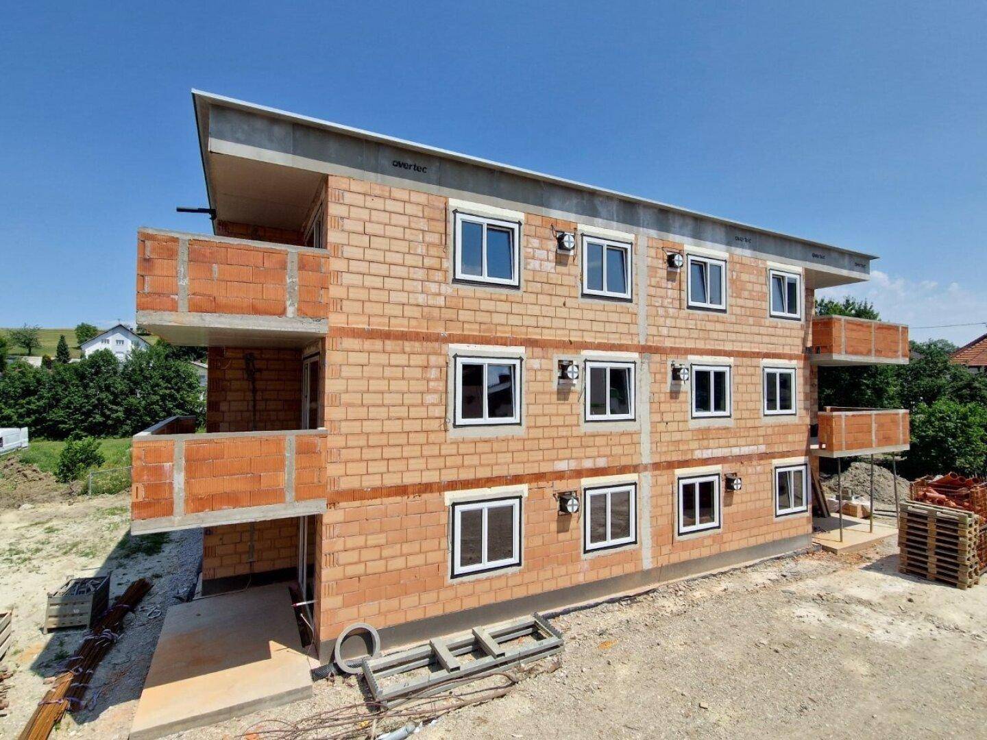 Neubau eines Mehrfamilienhauses im Rohbauzustand mit mehreren Balkonen und Fenstern.