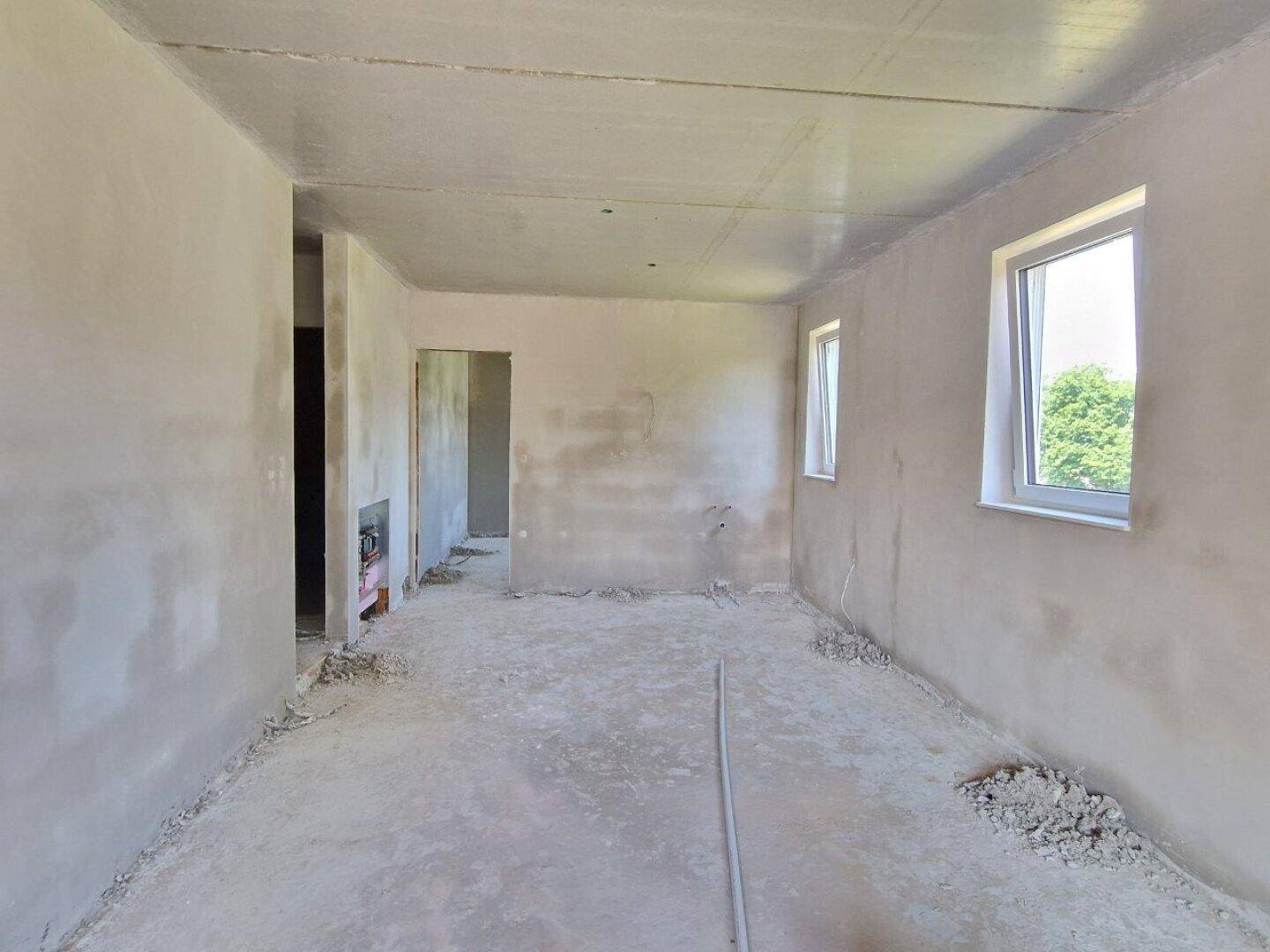 Unfertiger Innenraum mit rohen Wänden, Betonboden und Fenstern, bereit für den Ausbau.