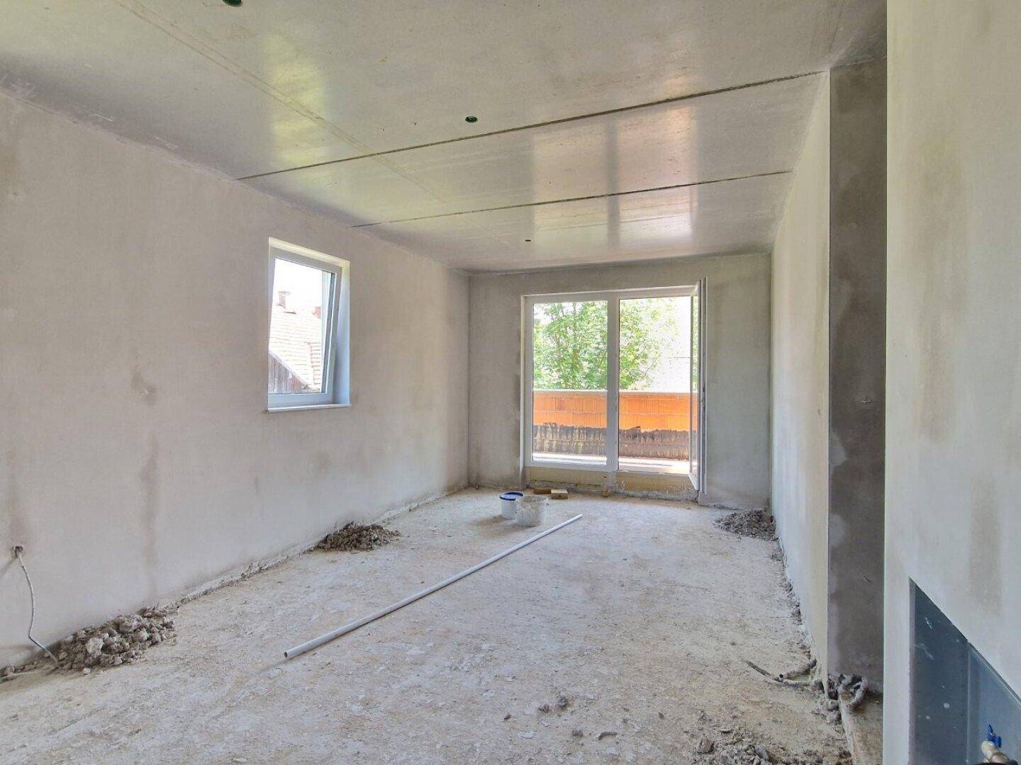 Heller Rohbau-Raum mit großem Fenster und Zugang zu einem potenziellen Balkon oder Terrasse.