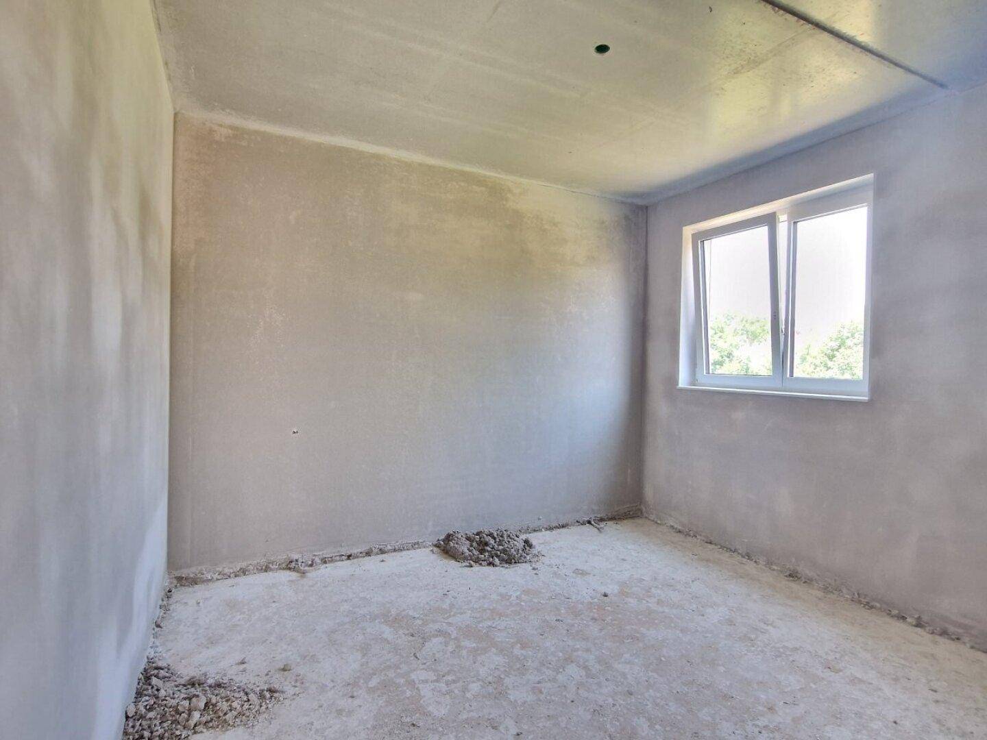 Einfacher Rohbau-Raum mit einem Fenster, das Tageslicht hereinlässt, im Bauzustand.