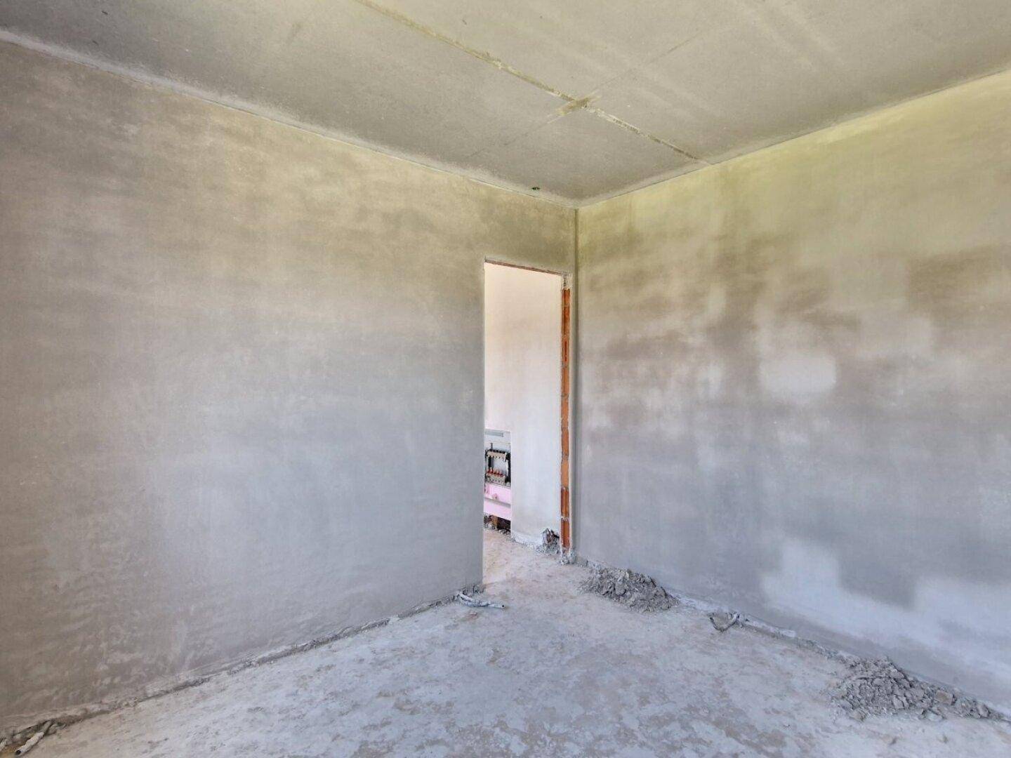 Unfertiger Innenraum mit einem Türrahmen, der zu einem weiteren Bereich führt, im Rohbau.