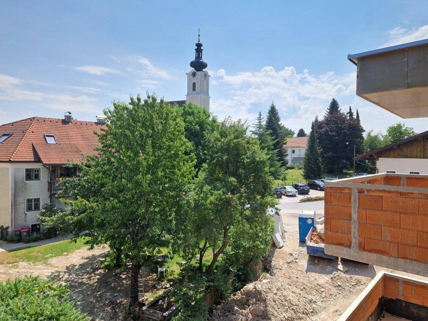Blick auf einen Kirchturm und umliegende Häuser, teilweise mit Baustelle im Vordergrund.