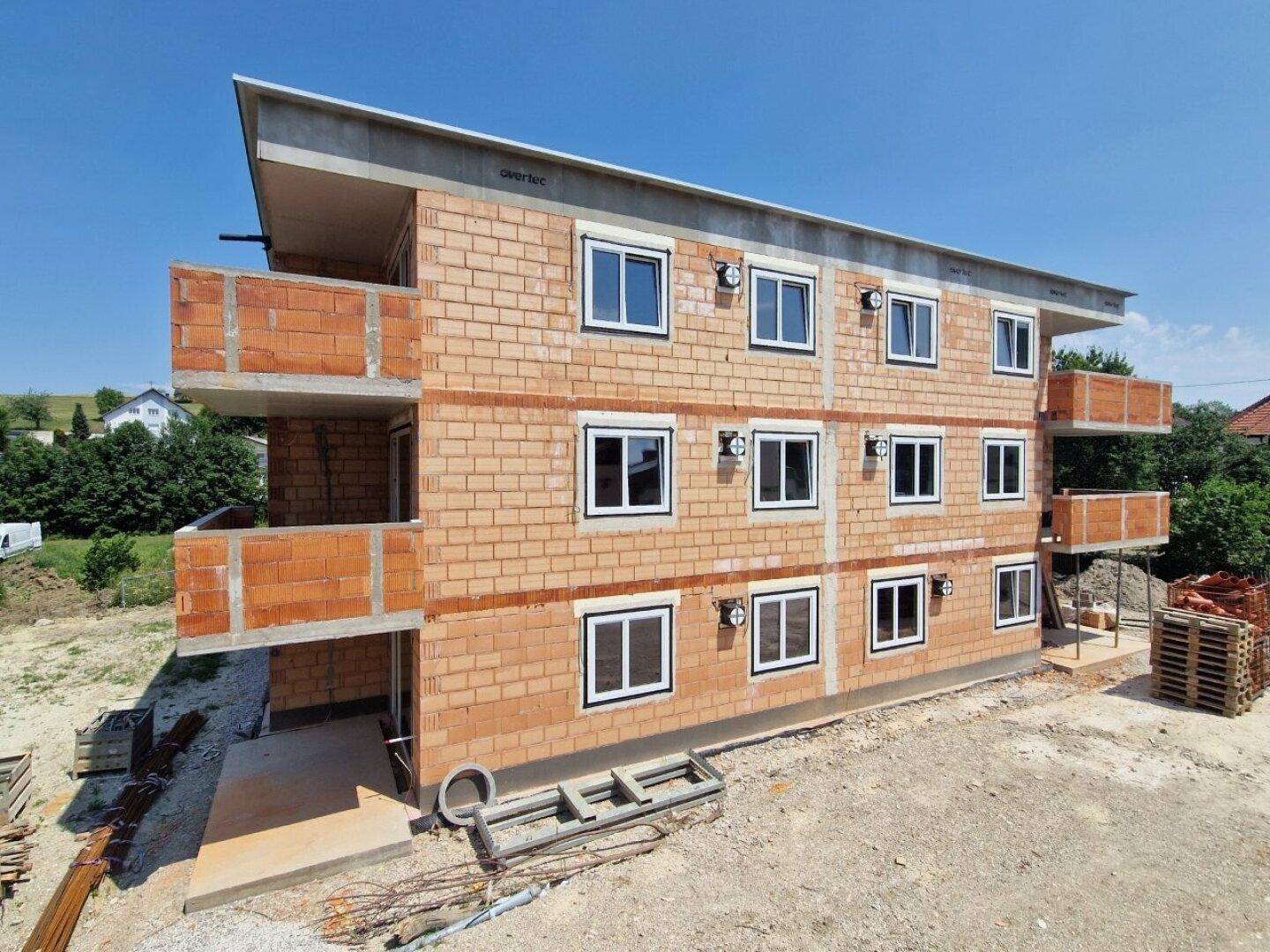 Seitenansicht eines neuen Wohngebäudes im Rohbau mit zahlreichen Fenstern und Balkonen.