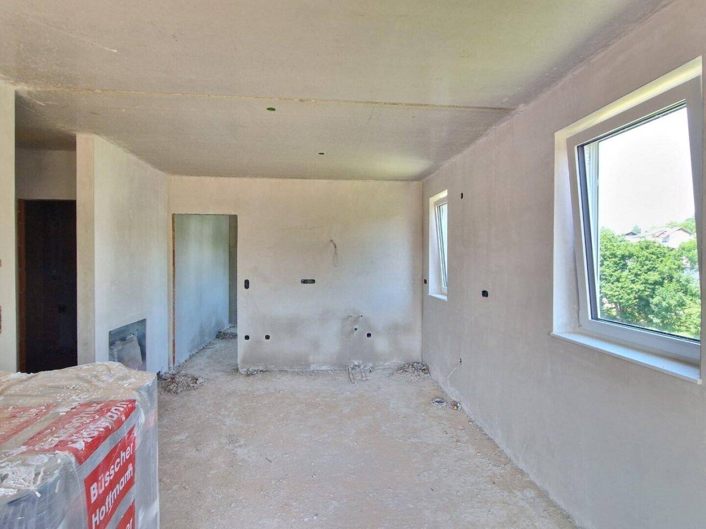 Unfertiger Innenraum eines Neubaus mit rohen Wänden, Betonboden und einem Fenster.