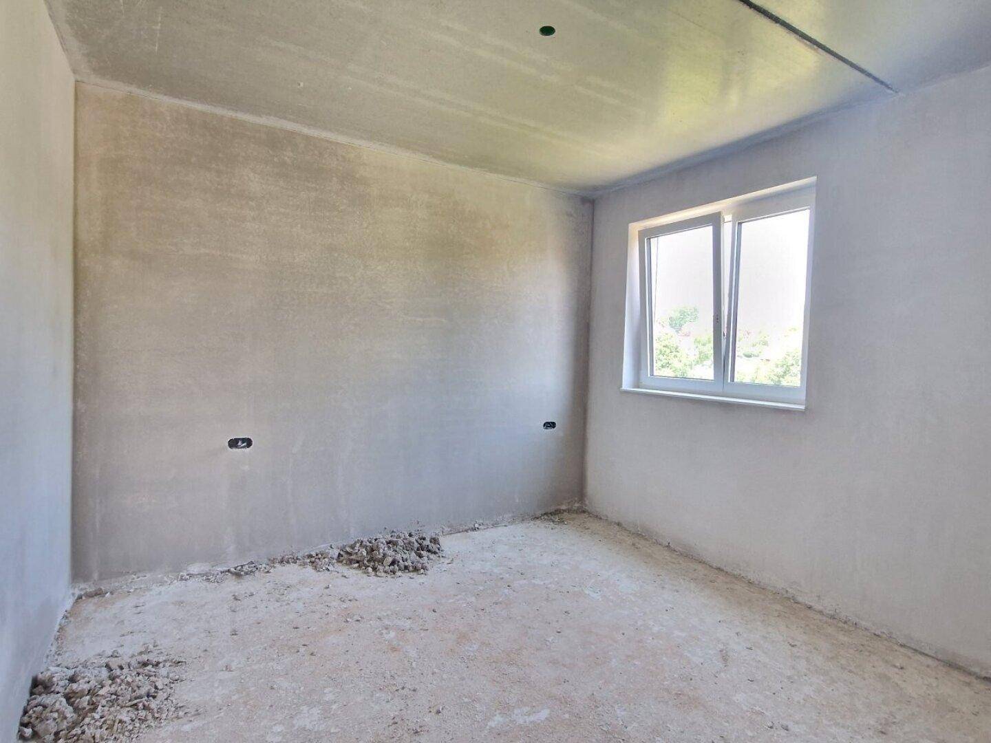Unfertiger Raum im Neubau mit einem Fenster und rohen Wänden, bereit für den Ausbau.