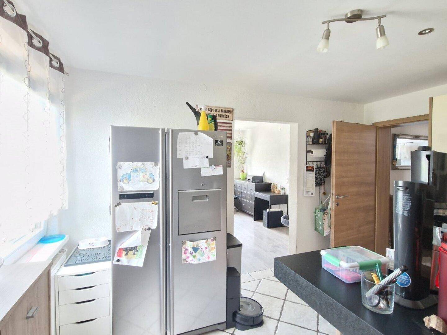 Küche mit großem Kühlschrank und Durchgang zu einem weiteren Wohnbereich.