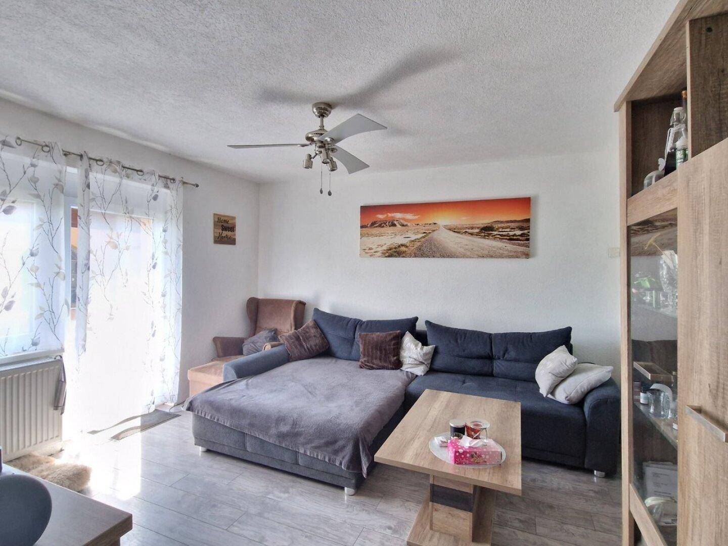 Gemütliches Wohnzimmer mit großem Sofa, Deckenventilator und hellem Boden.