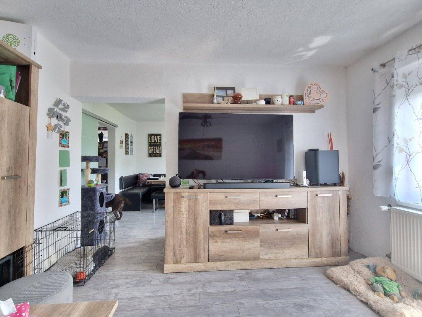 Wohnzimmer mit TV-Möbeln und offenem Zugang zu einem weiteren Raum.