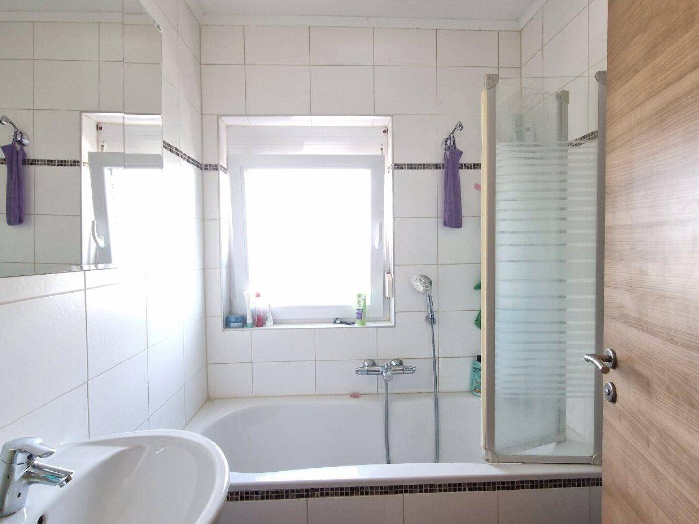 Helles Badezimmer mit Badewanne, Duschabtrennung und Fenster.