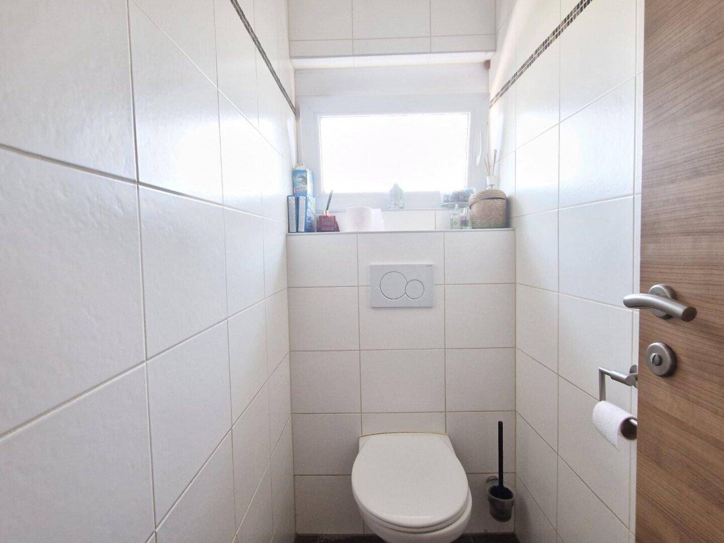 Separates WC mit wandhängender Toilette und kleinem Fenster.