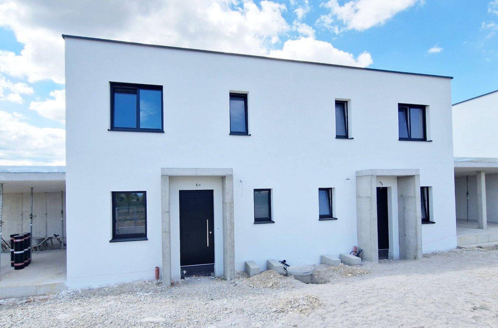 Vorderansicht eines Neubaus im Rohbauzustand mit modernen schwarzen Fenstern und Türen.