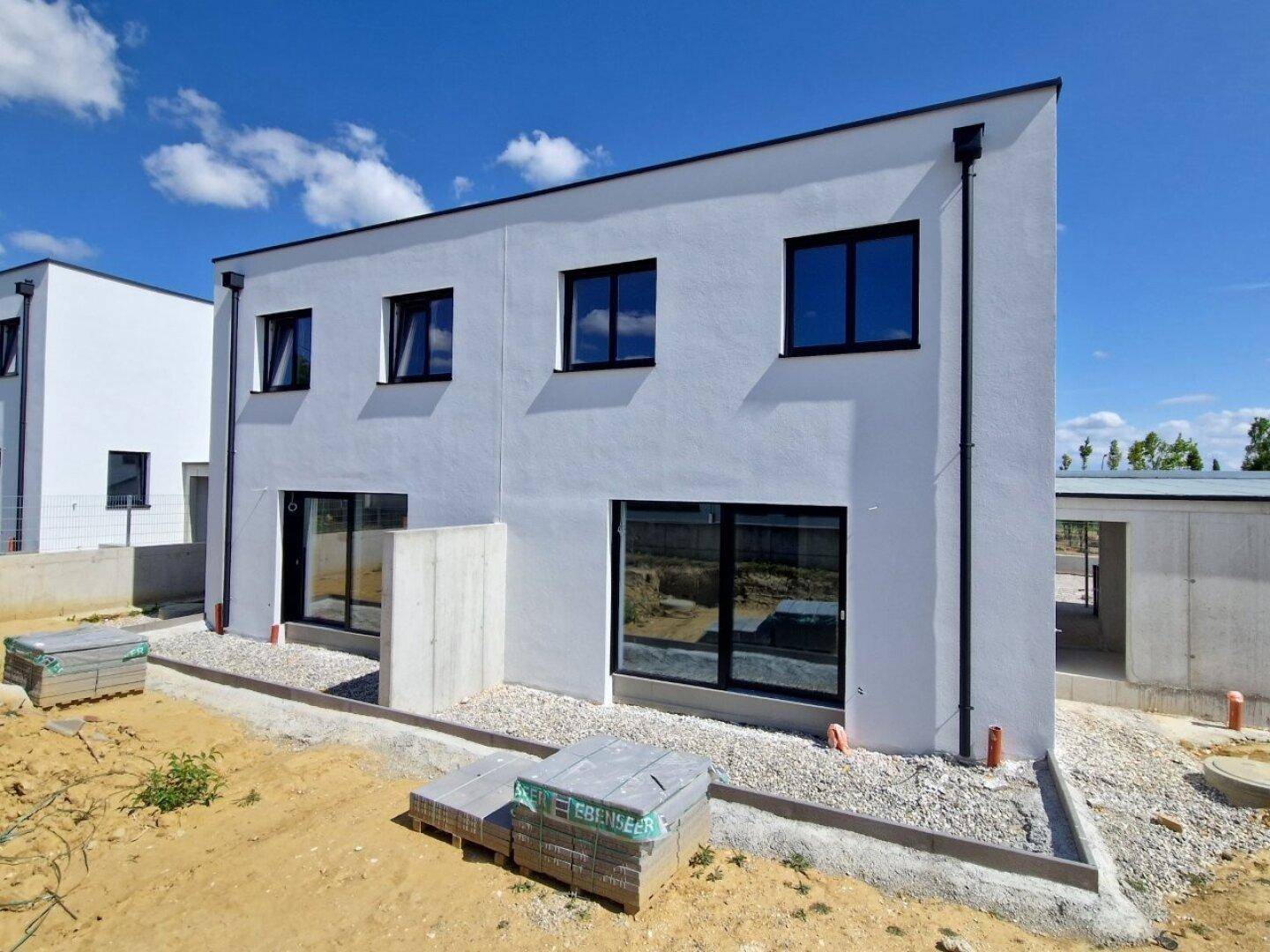 Seitenansicht eines modernen Neubaus mit großen Fensterfronten und Rohbauzustand der Fassade.