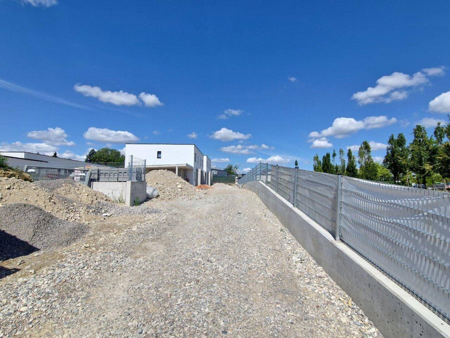 Baustelle einer neuen Wohnsiedlung mit vorbereiteten Grundstücken und Gebäuden im Hintergrund.