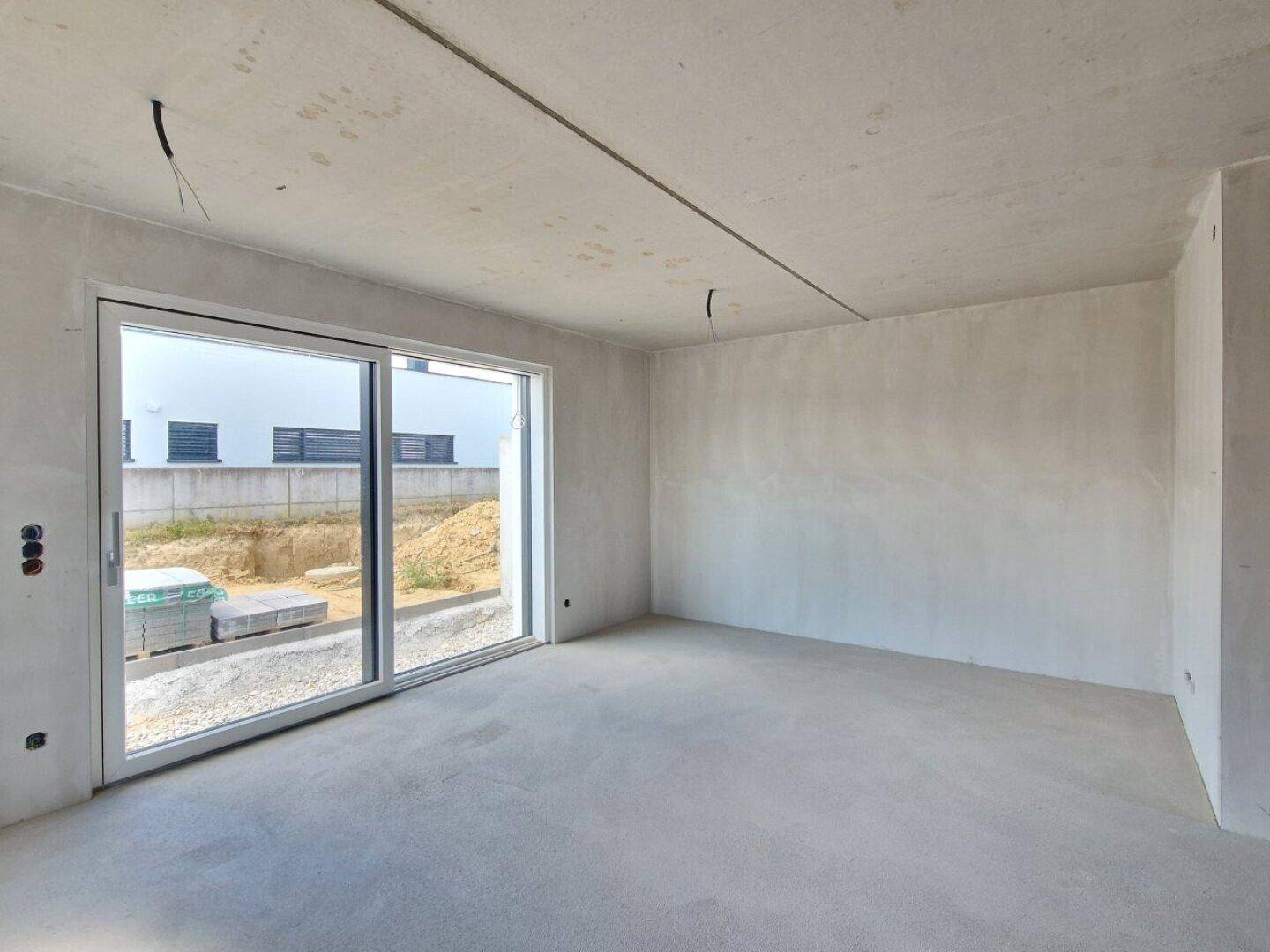 Heller Wohnraum im Rohbau mit großer Schiebetür und Blick auf die Baustelle.