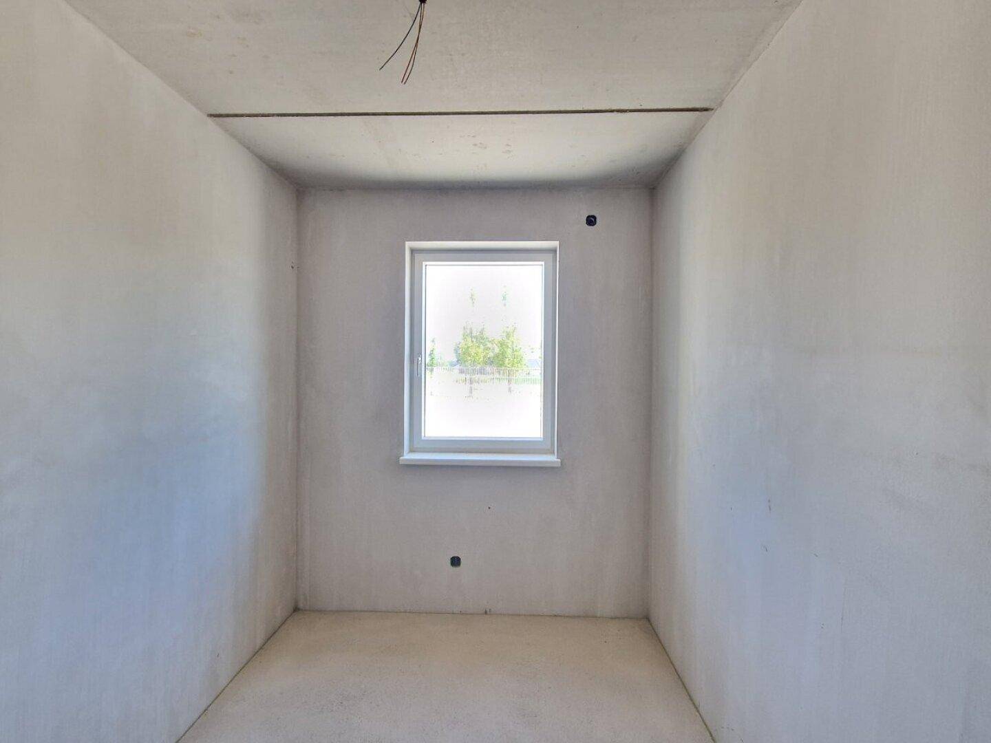 Schlafzimmer im Rohbau mit einem Fenster und unfertigen Wänden und Betonboden.
