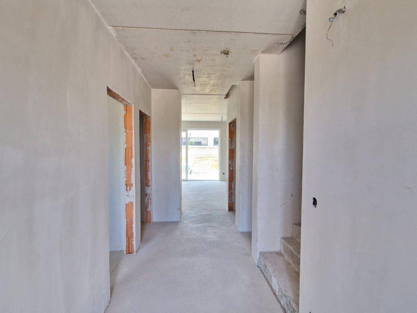 Langer Flur im Rohbau mit mehreren Türöffnungen und Betonboden im Neubau.