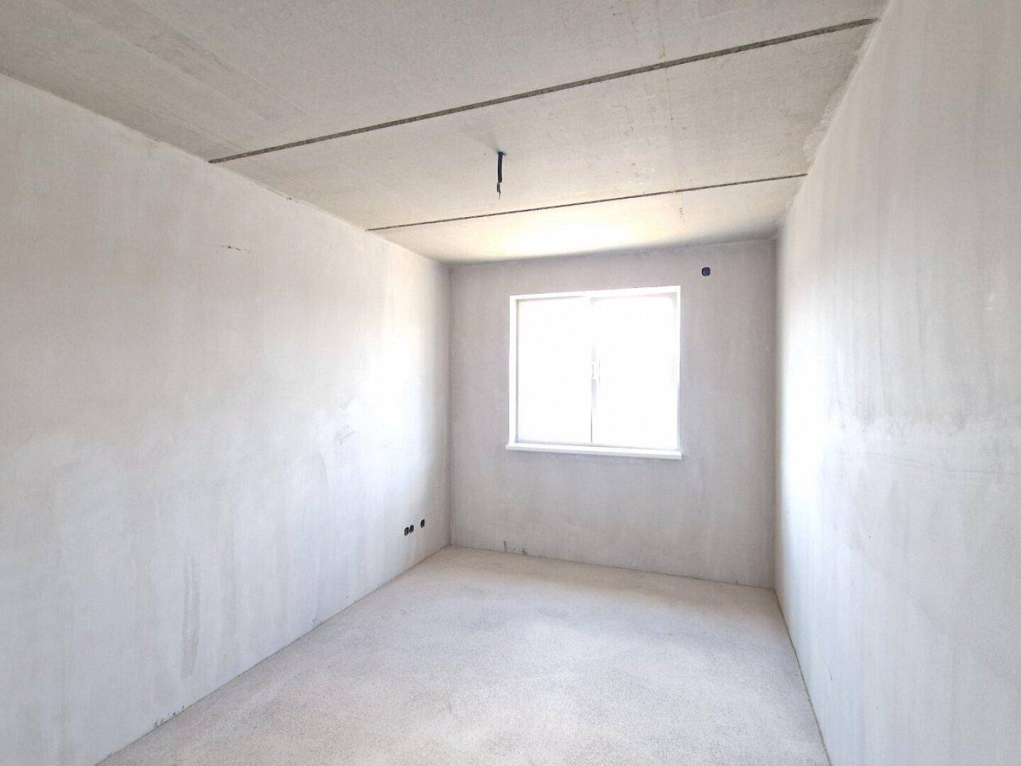 Schlafzimmer im Rohbau mit einem Fenster und unfertigen Wänden und Betonboden.