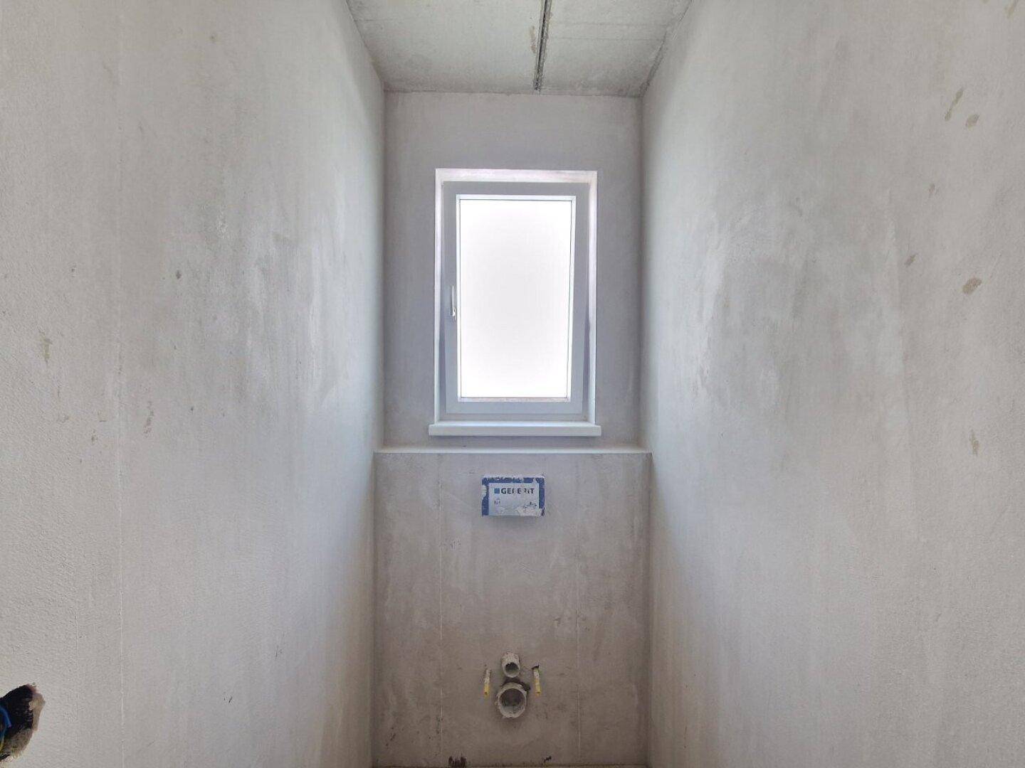 Kleiner Raum im Rohbau, vorbereitet für ein WC oder Gäste-WC mit Fenster.