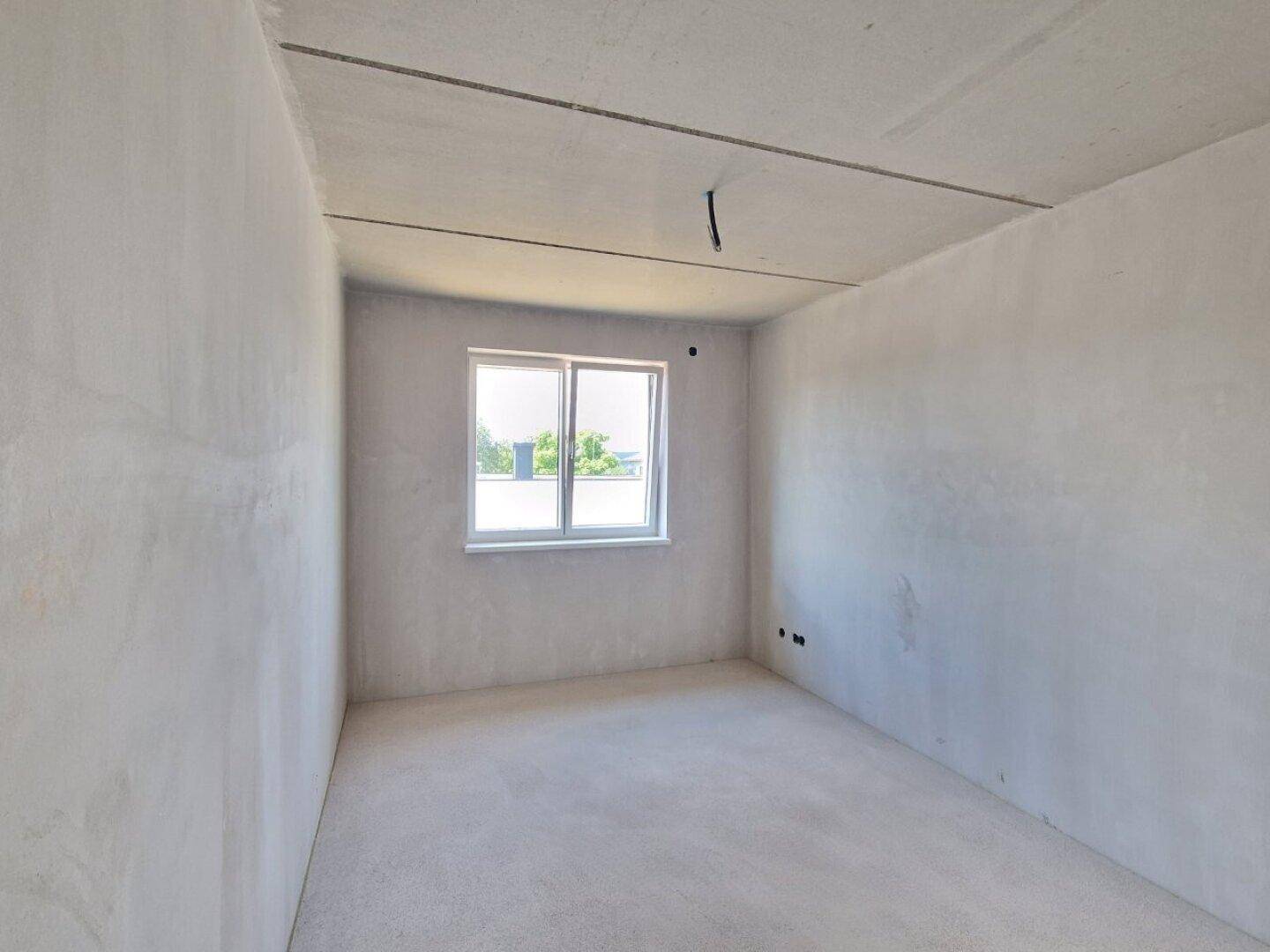 Helles Schlafzimmer im Rohbau mit Fenster und Blick ins Grüne von der Baustelle.