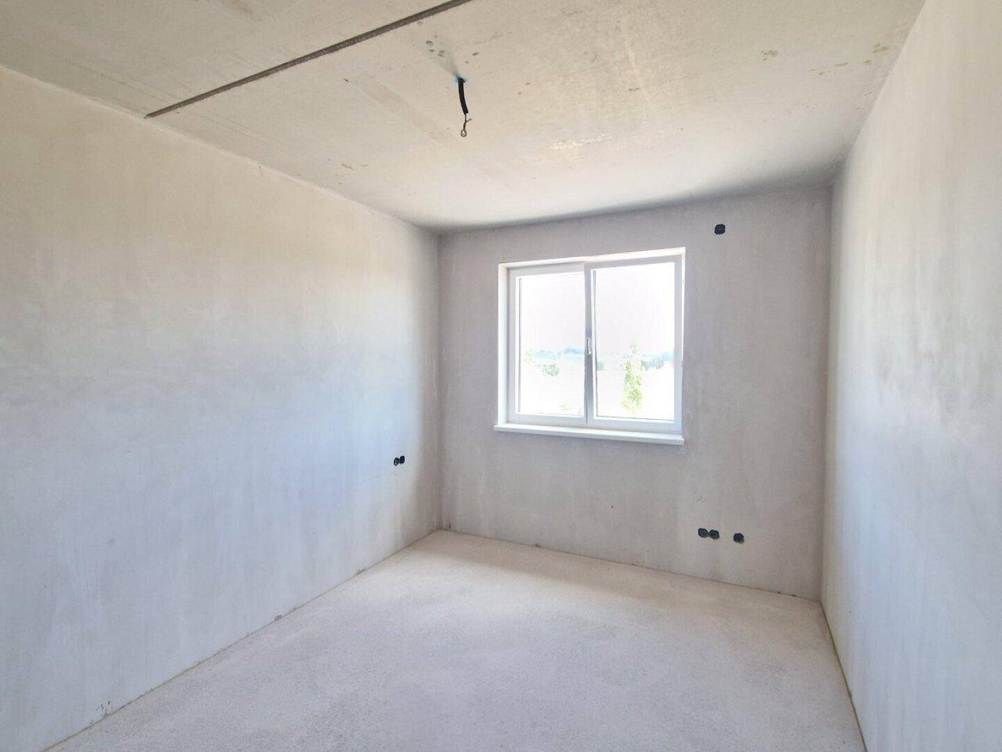 Geräumiges Schlafzimmer im Rohbau mit Fenster und unfertigen Wänden und Boden.