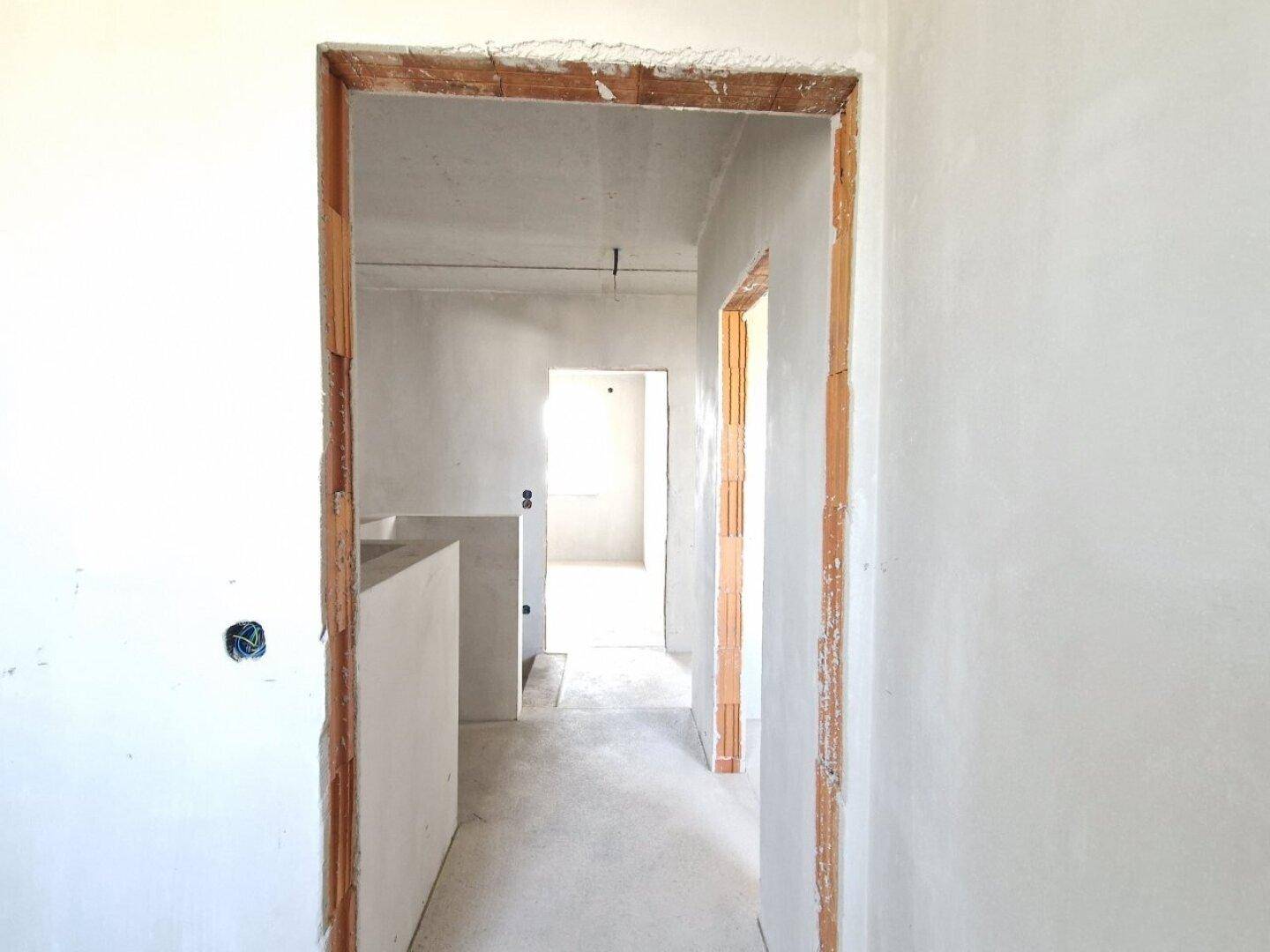 Flur im Rohbau mit Türöffnungen zu weiteren Räumen und Betonboden im Neubau.