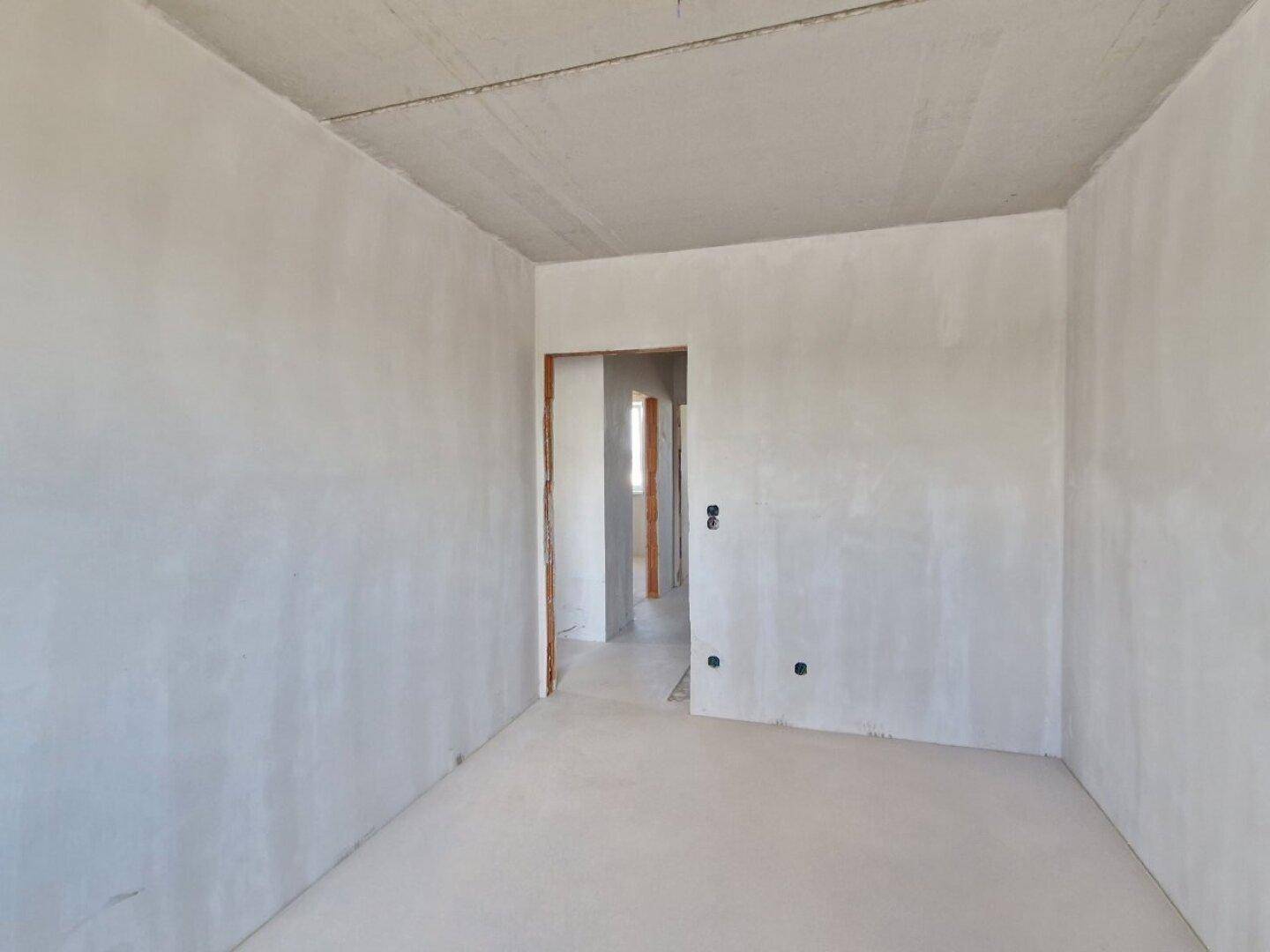 Leerer Raum im Rohbauzustand mit unverputzten Wänden und einfacher Betonfläche, wartet auf Fertigstellung.