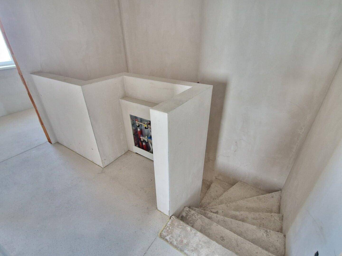 Unfertige Betontreppe in einem Rohbau, die in ein weiteres Stockwerk führt, mit kleiner Nische.