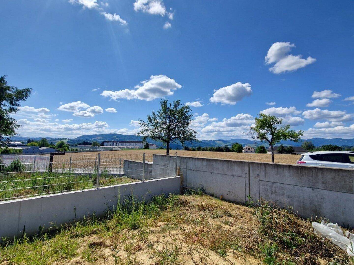 Offenes Grundstück mit Blick auf Felder und Berge, bereit für die Gestaltung des Außenbereichs.