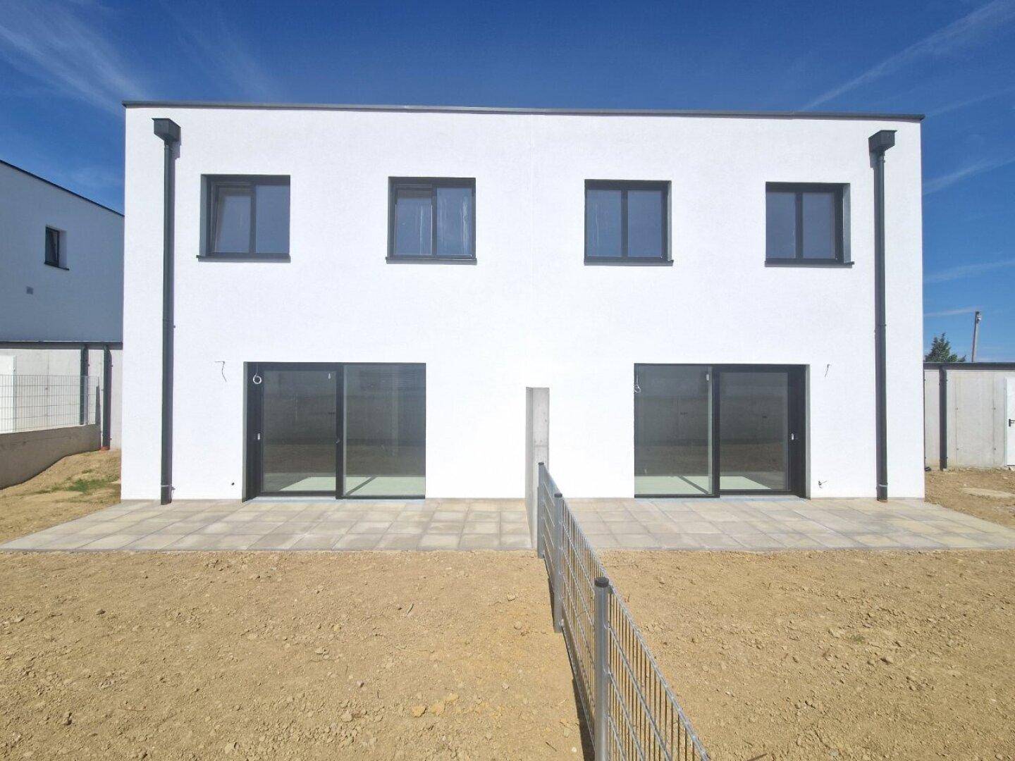 Rückansicht von zwei Neubauhäusern mit großen Schiebetüren und gepflasterten Terrassenbereichen.