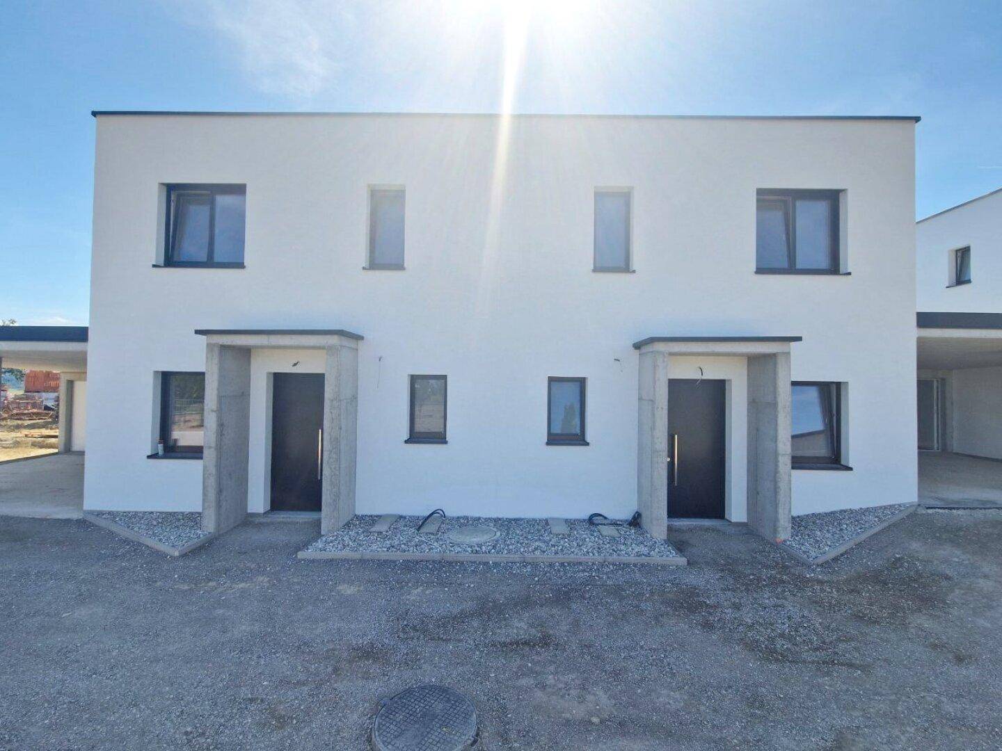 Frontale Ansicht von zwei modernen Neubauhäusern mit klaren Linien und dunklen Eingangstüren.