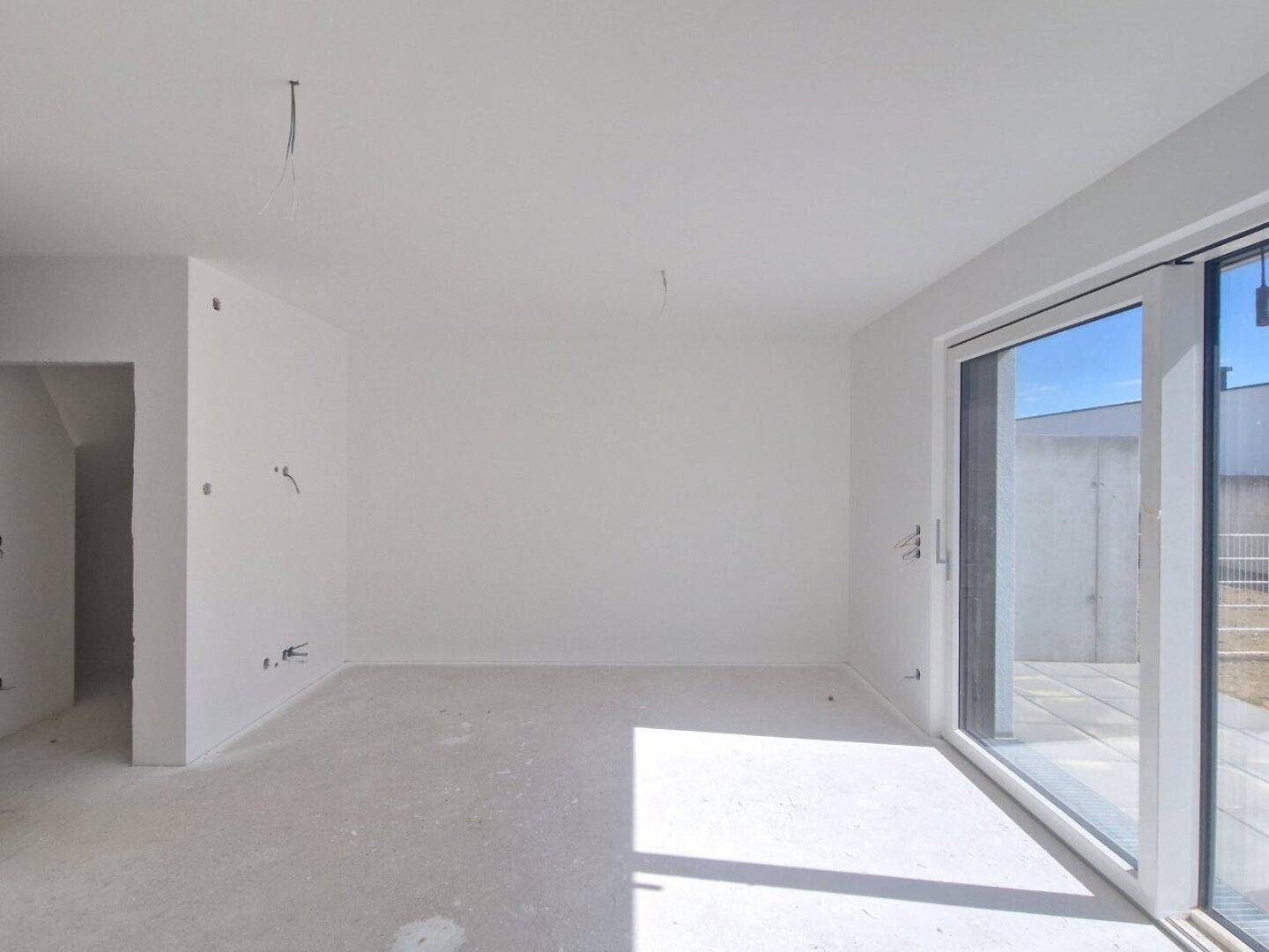 Heller, unfertiger Wohnraum mit großen Schiebetüren und Blick auf die zukünftige Terrasse.