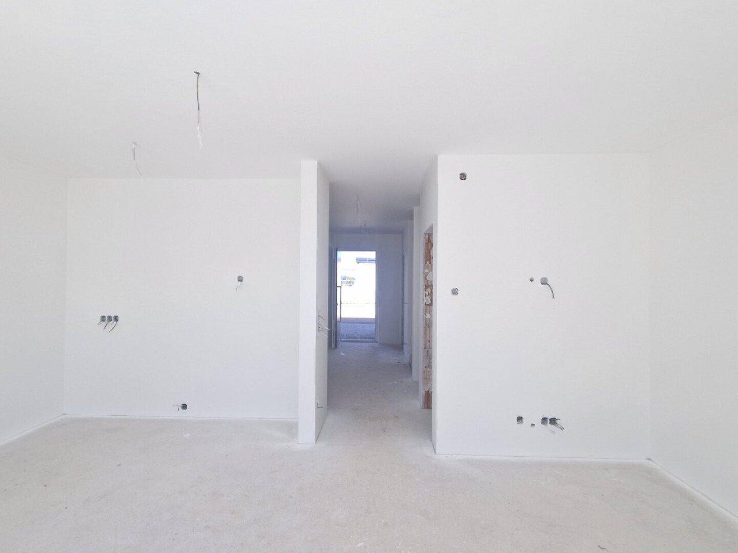 Heller Wohnraum im Rohbau mit Durchgang zu einem Flur, bereit für den Innenausbau.