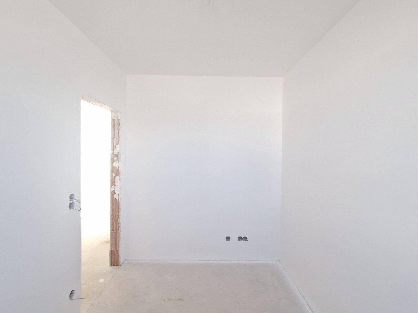 Unmöblierter Raum im Rohbau mit weiß gestrichenen Wänden und einem Türrahmen.