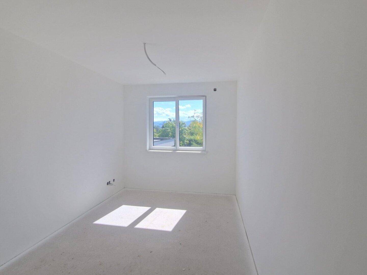 Heller Raum im Rohbau mit Fenster und einem schönen Blick ins Grüne.