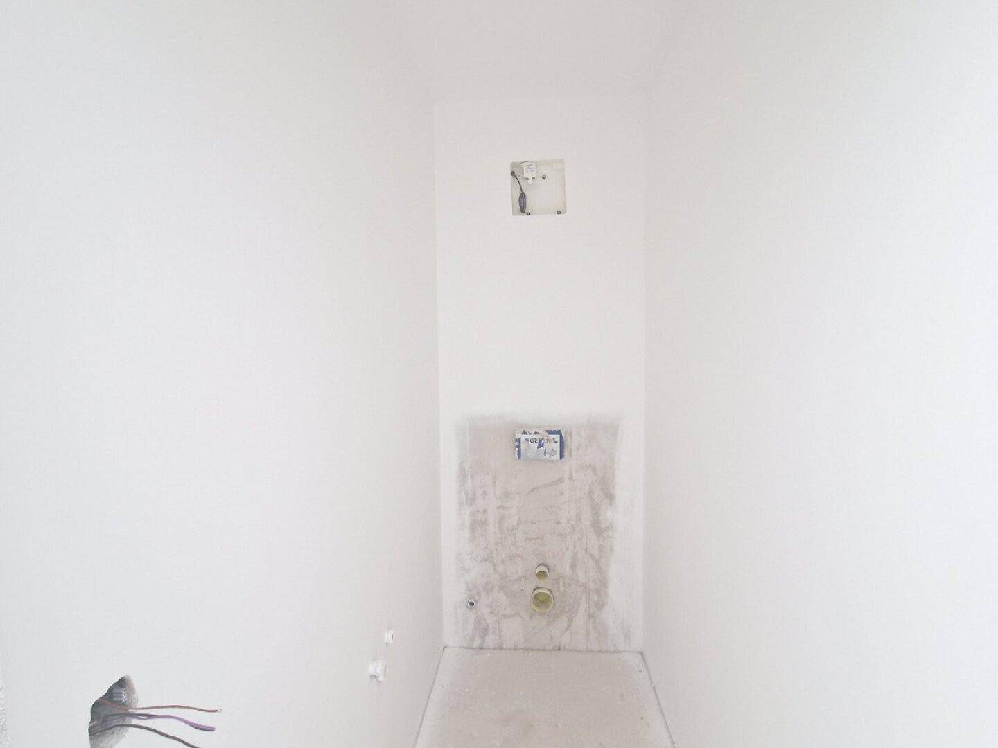 Kleiner Raum im Rohbau mit vorbereiteten Anschlüssen für ein Wand-WC.