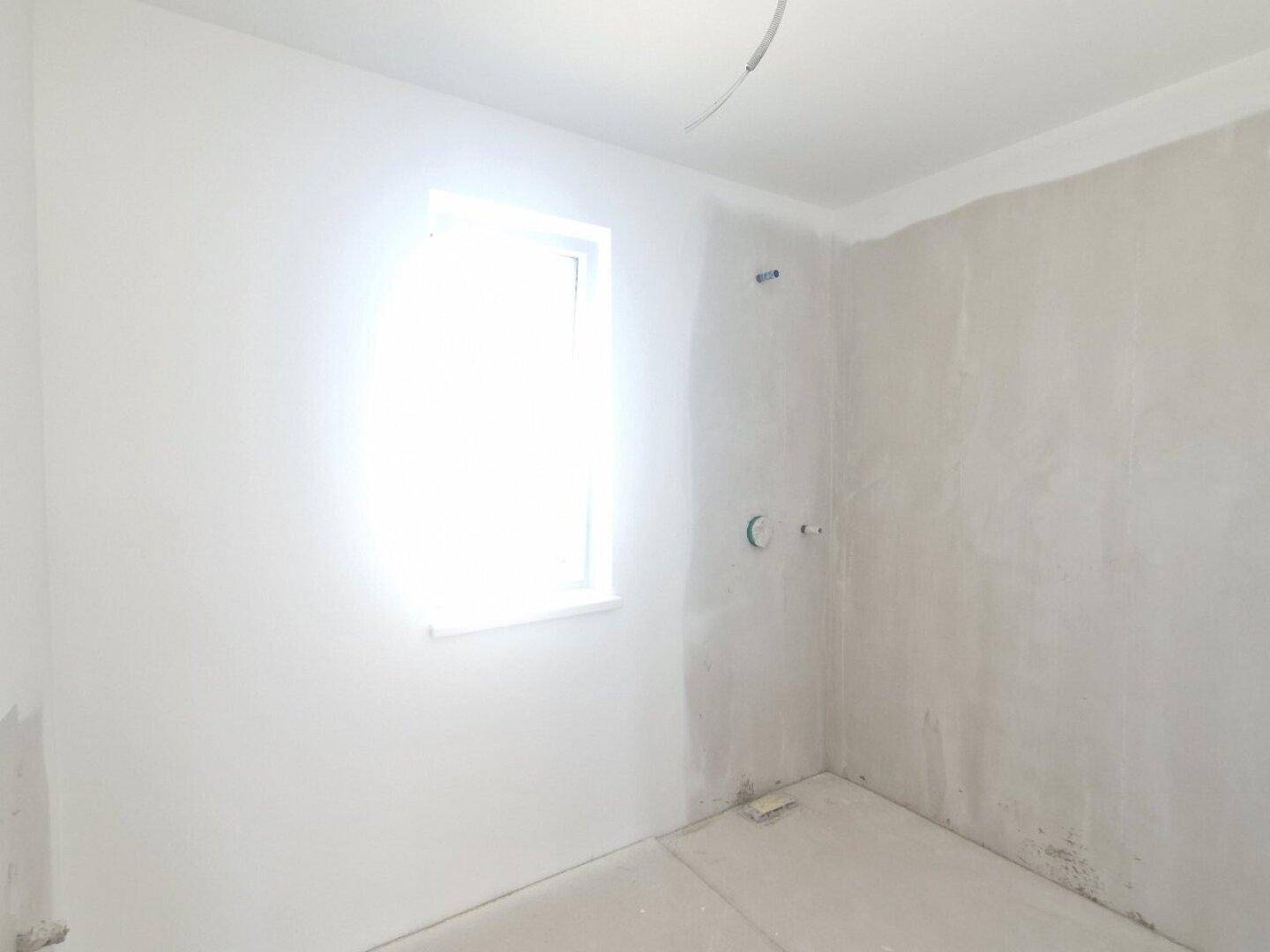Badezimmer im Rohbau mit Fenster und vorbereiteten Anschlüssen für Sanitärinstallationen.